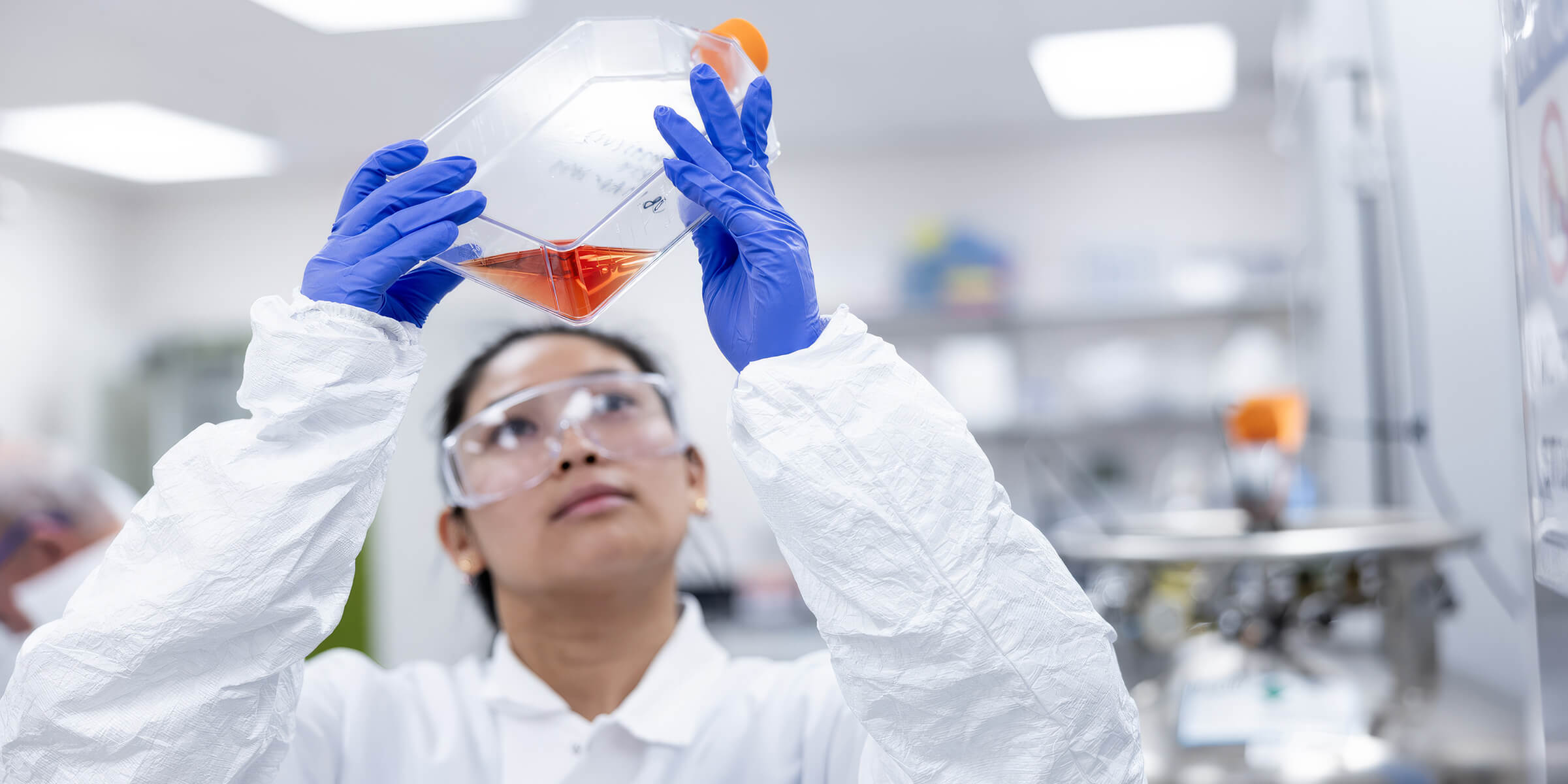 Lab technician inspecting a culture flask in a clean, modern lab.